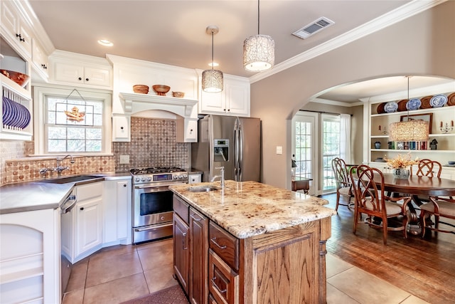 kitchen with a kitchen island with sink, stainless steel appliances, hardwood / wood-style floors, pendant lighting, and white cabinetry