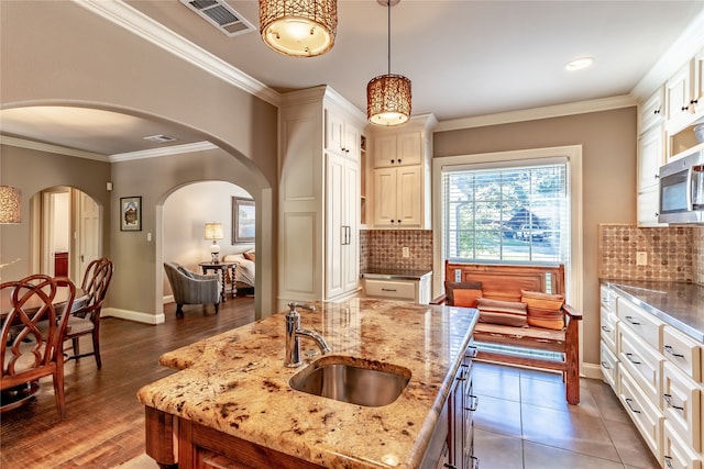 kitchen featuring sink, dark hardwood / wood-style flooring, hanging light fixtures, decorative backsplash, and a center island with sink