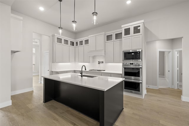 kitchen with white cabinets, appliances with stainless steel finishes, light hardwood / wood-style flooring, sink, and a center island with sink