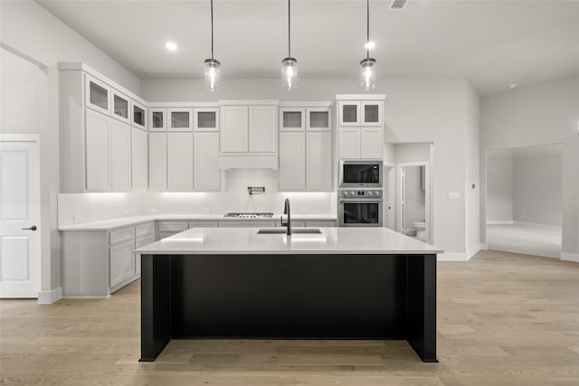 kitchen featuring white cabinetry, an island with sink, sink, stainless steel oven, and built in microwave