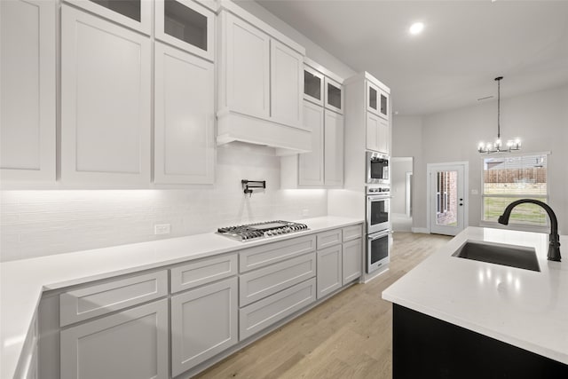 kitchen featuring decorative light fixtures, sink, light hardwood / wood-style flooring, stainless steel appliances, and white cabinets