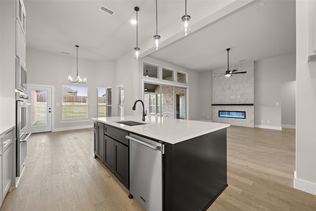 kitchen featuring appliances with stainless steel finishes, light hardwood / wood-style floors, a large fireplace, hanging light fixtures, and a center island with sink