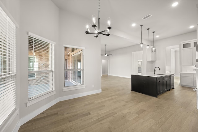 kitchen with white cabinetry, light hardwood / wood-style floors, sink, hanging light fixtures, and a center island with sink