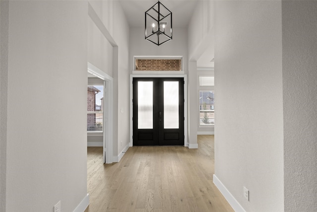 foyer entrance with light hardwood / wood-style floors, a high ceiling, french doors, and an inviting chandelier