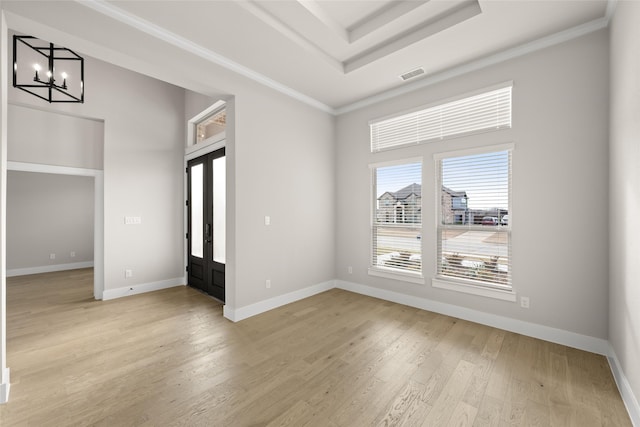 spare room with a raised ceiling, a chandelier, ornamental molding, and light hardwood / wood-style floors