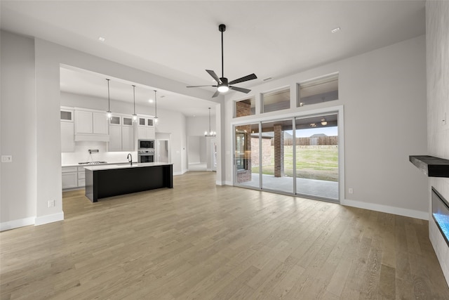 kitchen with pendant lighting, white cabinets, a kitchen island with sink, light wood-type flooring, and built in microwave