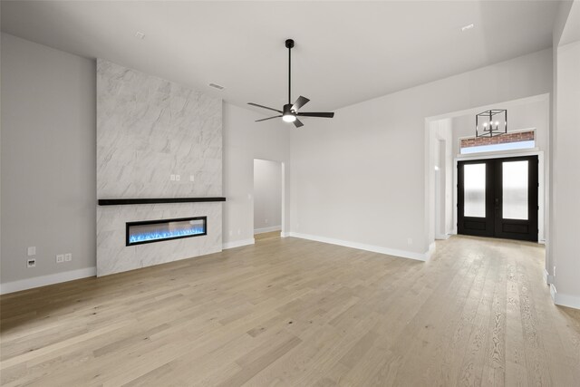 unfurnished living room featuring ceiling fan with notable chandelier, a towering ceiling, french doors, a fireplace, and light wood-type flooring