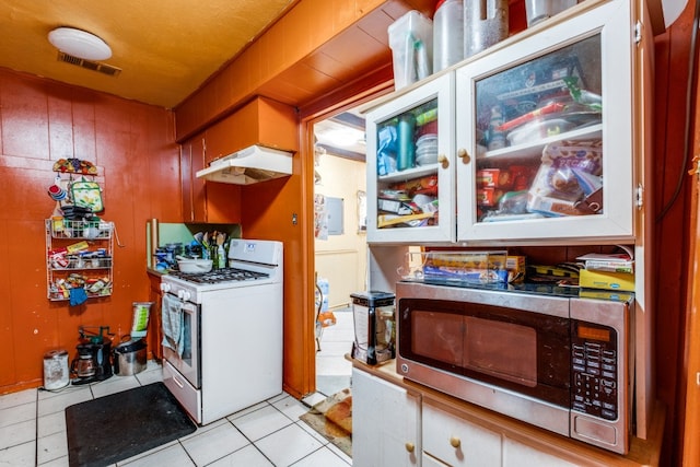 kitchen featuring white cabinetry, white gas stove, light tile patterned flooring, and wooden walls