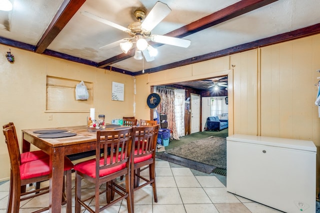 tiled dining area featuring wood walls, beamed ceiling, and ceiling fan