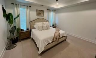 bedroom with a raised ceiling, ceiling fan, and light colored carpet