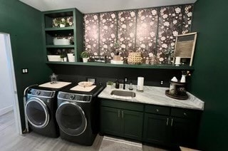 laundry area featuring cabinets, light wood-type flooring, sink, and washing machine and clothes dryer