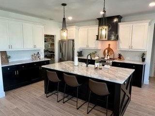 kitchen with a kitchen bar, stainless steel fridge, light hardwood / wood-style flooring, white cabinetry, and an island with sink