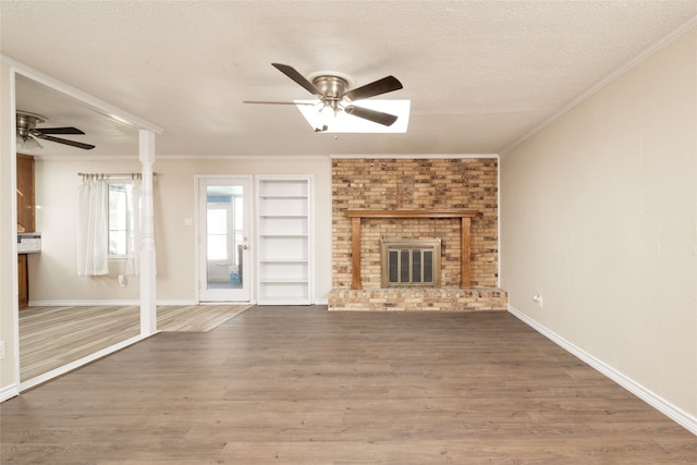 unfurnished living room featuring ceiling fan, wood-type flooring, a textured ceiling, and a brick fireplace