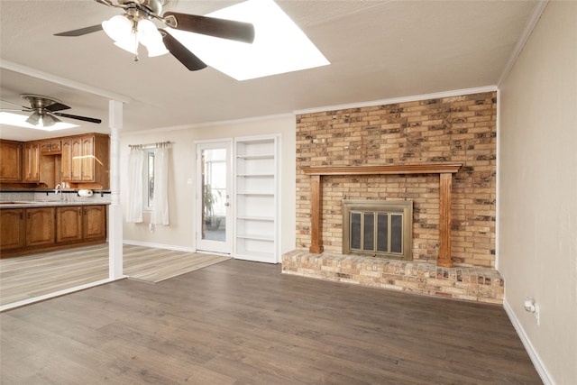 unfurnished living room featuring a brick fireplace, ornamental molding, wood-type flooring, and ceiling fan