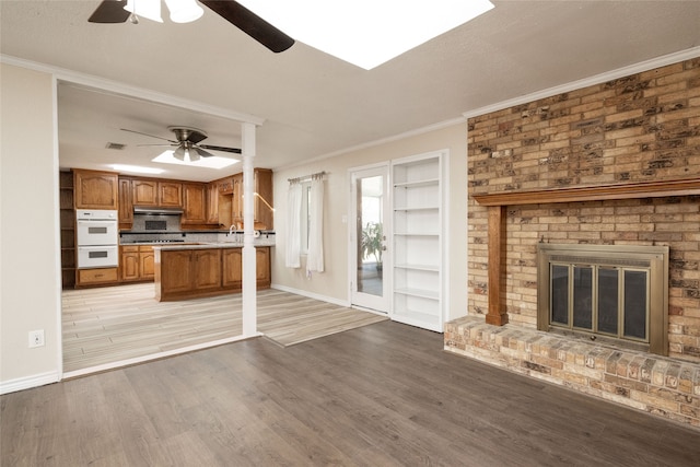 unfurnished living room with light hardwood / wood-style flooring, ornamental molding, a brick fireplace, and ceiling fan