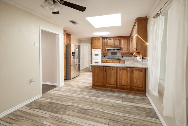 kitchen with white double oven, kitchen peninsula, sink, stainless steel fridge with ice dispenser, and ceiling fan