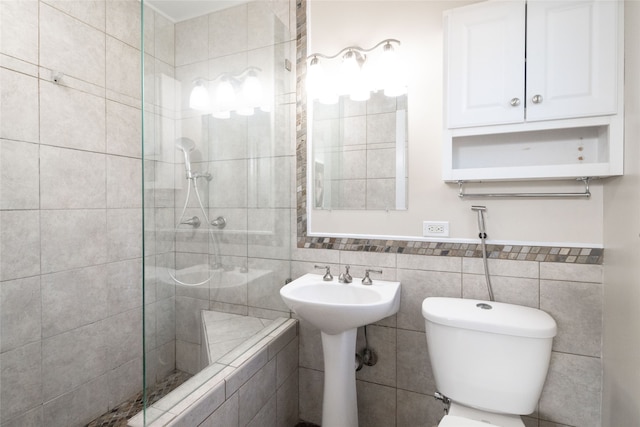 bathroom featuring tile walls, tiled shower, sink, and toilet