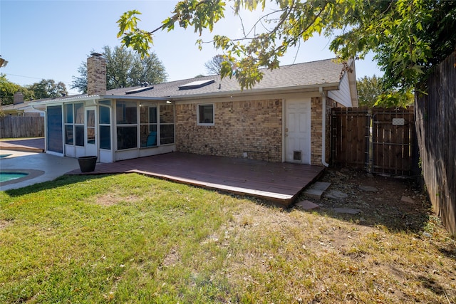 rear view of property featuring a sunroom, a deck, and a lawn