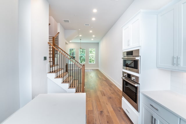 kitchen featuring backsplash, hanging light fixtures, light hardwood / wood-style flooring, and white cabinets