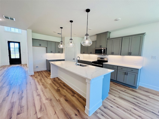 kitchen with light stone countertops, a kitchen island with sink, light hardwood / wood-style flooring, sink, and stainless steel appliances