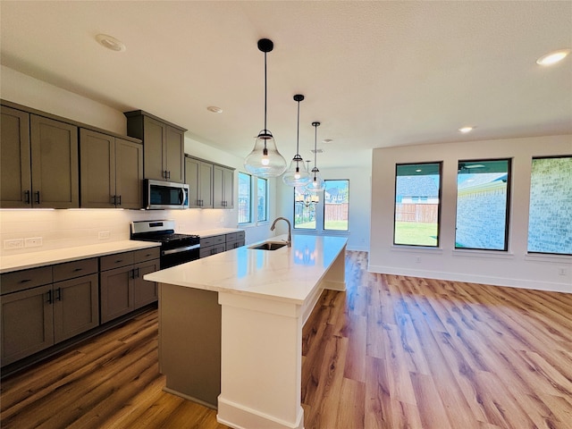 kitchen featuring light stone countertops, hanging light fixtures, stainless steel appliances, and light hardwood / wood-style floors