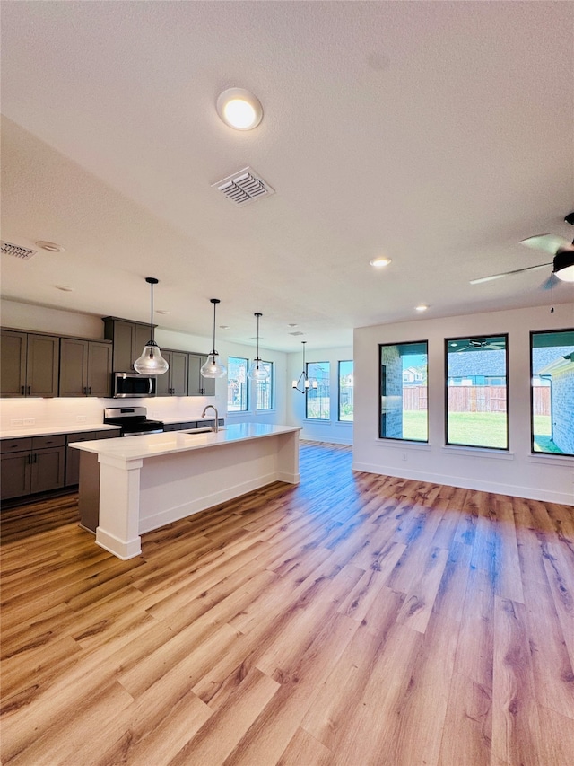 kitchen featuring a kitchen island with sink, pendant lighting, light hardwood / wood-style floors, and stainless steel appliances