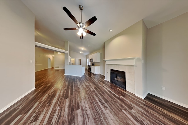 unfurnished living room featuring dark wood-type flooring, vaulted ceiling, a tile fireplace, and ceiling fan