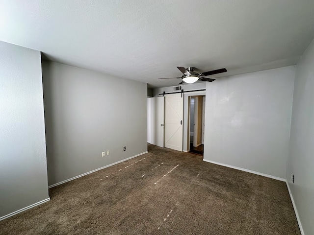 unfurnished bedroom featuring dark colored carpet, a barn door, and ceiling fan