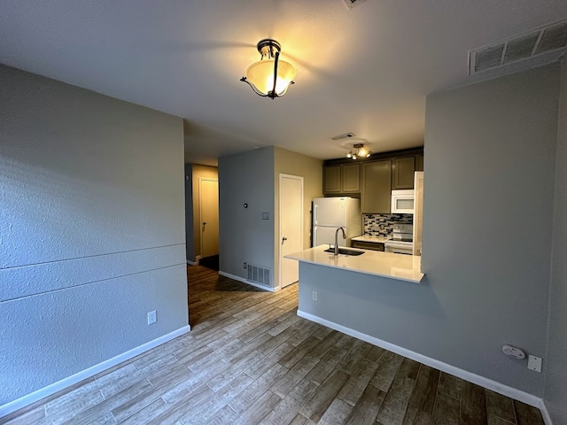 kitchen with kitchen peninsula, tasteful backsplash, dark wood-type flooring, sink, and white appliances