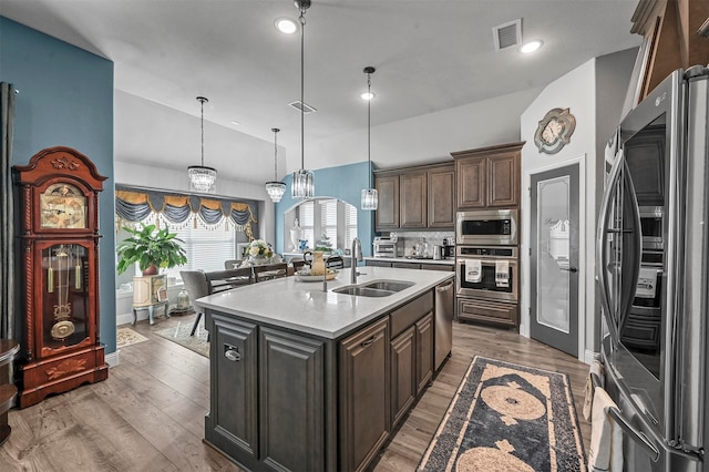 kitchen with a center island with sink, appliances with stainless steel finishes, hardwood / wood-style flooring, sink, and decorative light fixtures