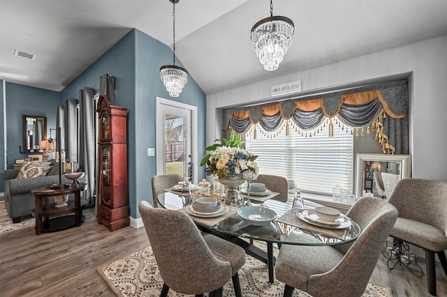 dining space with hardwood / wood-style flooring, lofted ceiling, and an inviting chandelier