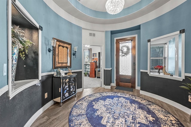 entryway with a notable chandelier, hardwood / wood-style flooring, and a tray ceiling