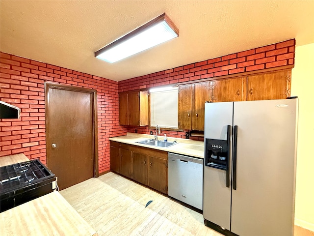 kitchen featuring brick wall, a textured ceiling, stainless steel appliances, sink, and light hardwood / wood-style flooring