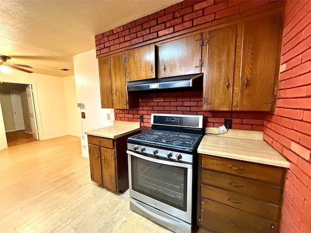 kitchen with a textured ceiling, light hardwood / wood-style floors, ceiling fan, and stainless steel range with gas stovetop