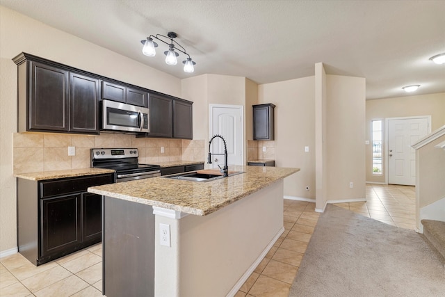 kitchen featuring tasteful backsplash, sink, light tile patterned flooring, an island with sink, and stainless steel appliances