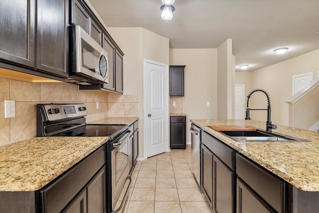 kitchen featuring appliances with stainless steel finishes, sink, light stone counters, decorative backsplash, and a center island with sink