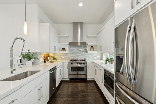 kitchen with sink, hanging light fixtures, white cabinetry, stainless steel appliances, and wall chimney exhaust hood