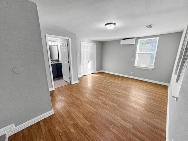 unfurnished bedroom featuring light hardwood / wood-style flooring, a textured ceiling, ensuite bath, and an AC wall unit