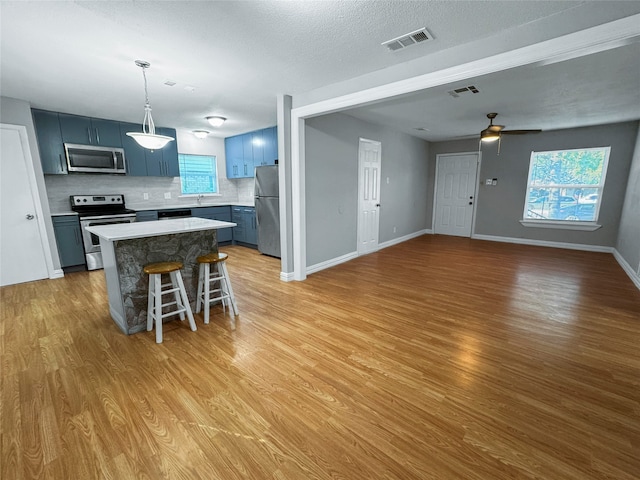 kitchen featuring light wood-type flooring, stainless steel appliances, pendant lighting, decorative backsplash, and a breakfast bar