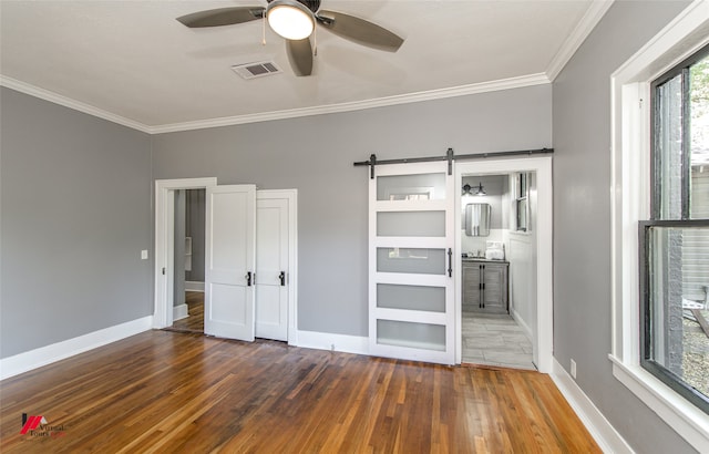 unfurnished bedroom featuring ensuite bath, a barn door, dark hardwood / wood-style floors, and ceiling fan