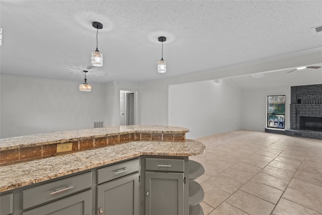 kitchen featuring a textured ceiling, light stone countertops, a brick fireplace, and pendant lighting