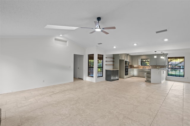 unfurnished living room featuring lofted ceiling with skylight, light tile patterned floors, plenty of natural light, and ceiling fan