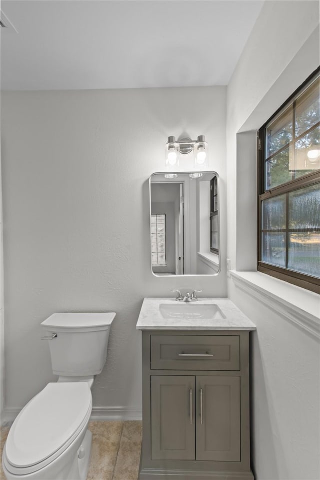 half bathroom featuring toilet, tile patterned floors, vanity, and baseboards