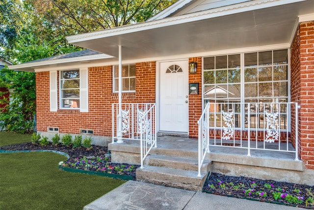 entrance to property with covered porch and a yard