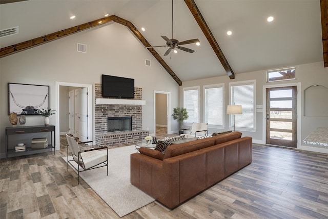 living room with beam ceiling, ceiling fan, high vaulted ceiling, a fireplace, and light hardwood / wood-style floors