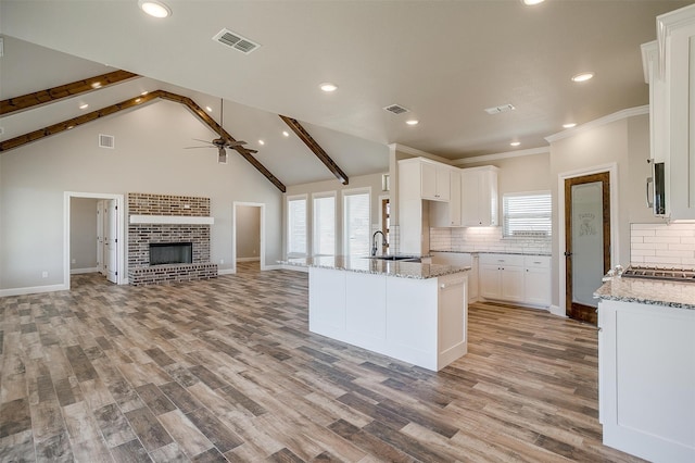 kitchen featuring light stone counters, white cabinets, vaulted ceiling with beams, and light hardwood / wood-style flooring