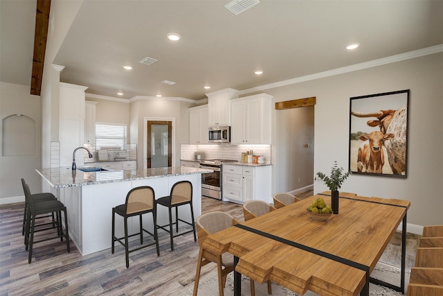 kitchen featuring appliances with stainless steel finishes, sink, light wood-type flooring, white cabinetry, and light stone counters