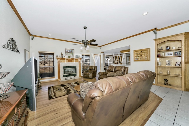 living room featuring ornamental molding, ceiling fan, a tile fireplace, built in features, and light hardwood / wood-style floors