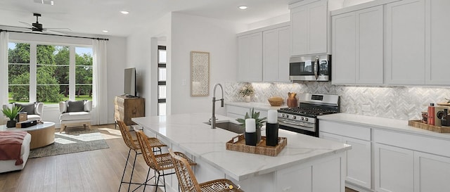 kitchen with an island with sink, sink, white cabinets, appliances with stainless steel finishes, and light hardwood / wood-style floors