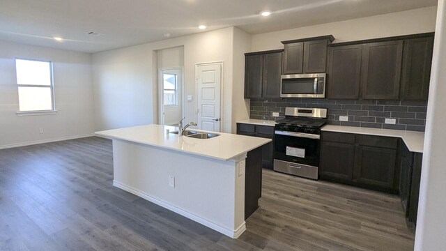 kitchen with backsplash, stainless steel appliances, dark wood-type flooring, sink, and a center island with sink